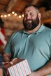 © Andrii Zastrozhnov - Smiling bearded man holding wrapped gift in cozy rustic interior for holiday celebration background and seasonal event use