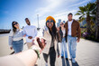 © CarlosBarquero - Follow me style travel scene with a cheerful Black woman holding the viewer's hand while friends stand behind in a bright modern neighborhood. Blue sky