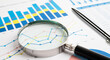 © Tanbir - Magnifying glass examining financial charts and business graphs with a black pen on a desk magnifying financial