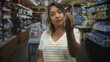 © Krakenimages.com - Woman beckoning with hand while touching temple in store aisle inside building, pensive expression and lifted fingers; concern hesitation.