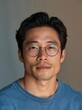 © CYBERPINK - Close-up portrait of a young asian man. he is wearing a blue t-shirt and has a pair of round, gold-framed glasses on.