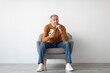 © Prostock-studio - Pensive Elderly Caucasian Man Seated Comfortably In Modern Armchair, Using Smartphone And Reflecting On Personal Matters, Shows Focused Emotion In Minimalistic Living Room Setting.