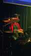 © VeNN - Drummer in red shirt green overalls plays cymbals under warm spotlight against dark green curtain. Dynamic composition with shallow depth of field. Mood is energetic focused