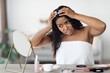 © Prostock-studio - Worried African American Woman Inspecting Her Scalp While Applying Hair Product In Front Of Mirror At Home, Showing Concern About Hair Health And Condition. Hair Care Concept.