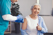 © Prostock-studio - Smiling Elderly Caucasian Woman Giving Thumbs Up While Receiving Vaccine From Nurse In Clinic Setting. Positive Emotion Displayed At Healthcare Appointment. Feeling Safe And Healthy.