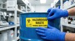 © Zaiseefa - Gloved hands for safety applying a hazardous waste drum safety label inside a sterile lab storage room.