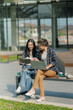 © MrAshi - Two Asian female college students using laptop with headphones while studying together on campus stairs.