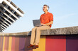 © VISTA by Westend61 - Man sits on a colorful wall in Barcelona and works on a laptop
