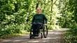 © Oleg - Smiling caucasian wheelchair user rolling along a paved path in a green forest. Disabled young female enjoying leisure time and active mobility in a summer park.