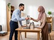 © Agus Through Lens - Cheerful muslim husband offering coffee mug to wife working on laptop at desk home office