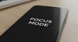 © xiden - Close up of a sleek modern smartphone resting on a wooden desk displaying white text focus mode for productivity and digital detox concepts
