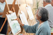 © Ekkasit A Siam - Senior Asian woman painting on canvas during creative art activity with other elderly residents in assisted living community, supporting mindfulness, social engagement, healthy aging and wellbeing.