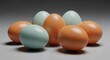 © Faizal - A group of seven glossy brown and pale blue chicken eggs arranged in a tight cluster on a smooth gray studio surface with soft lighting, subtle reflections, and neutral background.