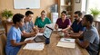 © Jakia Hossain  - Diverse healthcare team in scrubs gathered around wooden table reviewing paperwork, charts, and laptop screen in bright clinic office