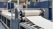 © pufanya - Industrial automated manufacturing line processing heavy embossed white linen textured wallpaper. Heavy machinery rollers and steel cylinders producing rolls of wall covering in modern factory