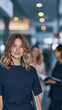 © pattozher - Confident Professional in the Hallway: A poised young woman with a warm smile confidently walks down a modern office hallway, with colleagues blurred in the background.