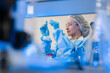 © VStudio - Focused female scientist in blue protective gown preparing a glass slide for microscopic analysis in sterile lab for clinical pathology, biotechnology research, and medical care.