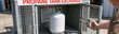 © pattozher - Propane Tank Exchange Service: A person opens a cage door to access a white propane tank for exchange, highlighting a convenient service for fuel needs.
