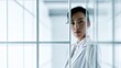 © koranis - A confident businesswoman in a white suit stands behind a glass partition, looking directly at the camera. The modern, minimalist office environment is reflected in the glass.