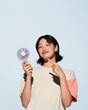 © Ryzhkov - Portable mini fan held by a smiling East Asian woman in a playful demonstration, featuring a matte finish and cotton knit, for marketplace