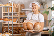 © JackF - Smiling Asian saleswoman holding a basket of fresh bread against the background of shelves with pastries. Seller offering fragrant bread in the baking section of a supermarket