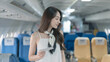 © ArLawKa - Asian woman passenger holding boarding pass ticket while looking for seat number in airplane cabin