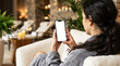 © MD Rashedul Islam - Hand holding mobile touchscreen phone with empty mockup screen, woman in grey bathrobe sitting on armchair in thermal spa relaxation lounge using hotel wellness reservation app