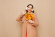 © Oleg Gekman - A beautiful young woman in a fashionable autumn outfit listens to music with wireless headphones. A girl in a stylish orange blouse poses on a beige background