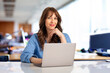 © sepy - Smiling businesswoman sitting with laptop in the office