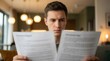 © Chayanan - Young man comparing financial insurance documents while reading carefully in an indoor setting.