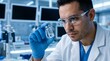© True Stock - Scientist in laboratory examines vial of liquid wearing protective glasses and gloves