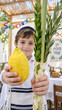 © olgakris - Boy in tallit presenting etrog plus lulav, jewish child standing inside decorated sukkah for holiday observance, family celebration article for seasonal faith gathering
