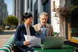 © Davor - Two business colleagues reviewing documents on laptop at outdoor cafe