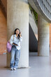 © iPoguz - Young asian female student listening to music with wireless headphones on modern campus hallway, happy student woman resting and enjoying music with headphones outside classroom