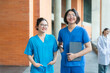 © iPoguz - Smiling young asian medical students wearing blue scrubs standing together at university hospital, happy healthcare interns holding tablet computer and posing outdoors at campus building