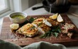 © maite - Filetes de pescado blanco al horno con costra de hierbas servidos en una tabla de madera con gajos de limón y salsa