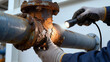 ©  VladaToday - Gloved maintenance worker illuminates severe corrosion on an aging industrial pipe joint for infrastructure inspection, equipment safety, repair planning and preventive maintenance