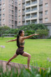 © leungchopan - Woman practicing warrior two yoga pose on grass outdoors