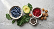 © Sasi - Flat lay top view of healthy superfoods assortment including blueberries, sliced avocado, pomegranate seeds, kale, chia seeds, and walnuts on grey stone background