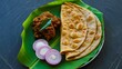 © MEE - Traditional Indian paratha served with spicy pickle and sliced red onion on a banana leaf, authentic South Asian cuisine