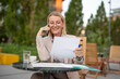 © Jelena - Mature businesswoman multitasking with phone call and paperwork outdoors