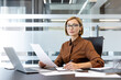 © Liubomir - Confident executive woman working at her desk, holding documents and writing notes, managing paperwork and responsibilities in a contemporary office environment