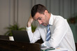 © Ekkasit A Siam - Concerned adult Caucasian businessman resting hand on forehead beside laptop in modern office, facing workplace stress and pressure while reviewing difficult project work and business problem.