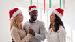 © AIMIN - Three diverse businesspeople in Santa hats dance together at an upbeat office Christmas celebration for marketing materials.