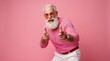 © Hungarian - Cheerful Stylish Senior Man with White Beard Pointing Finger Guns in Pink Sweater and Sunglasses on Pink Background