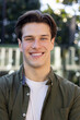 © Wavebreak Media - Man in 20s smiling, standing outside by glass railing, wearing white T-shirt and olive-green shirt