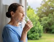 © Fabio_sc29 - Mature woman drinking a glass of water while looking out the window at a green garden