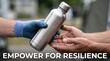 © Mitali Creative  - Person in blue work glove handing a stainless steel reusable water bottle to another person with open palms in an outdoor setting