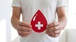 © MdNazrulIslam - A person in a white shirt holding a red paper blood drop with a white cross symbol representing health care and blood donation