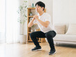 © Wasabi - リビングでスクワットの筋トレをする男性、明るい健康習慣の風景